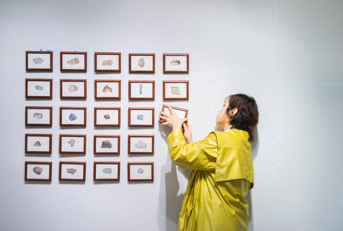 A person arranging small framed pieces on a gallery wall during an exhibition install