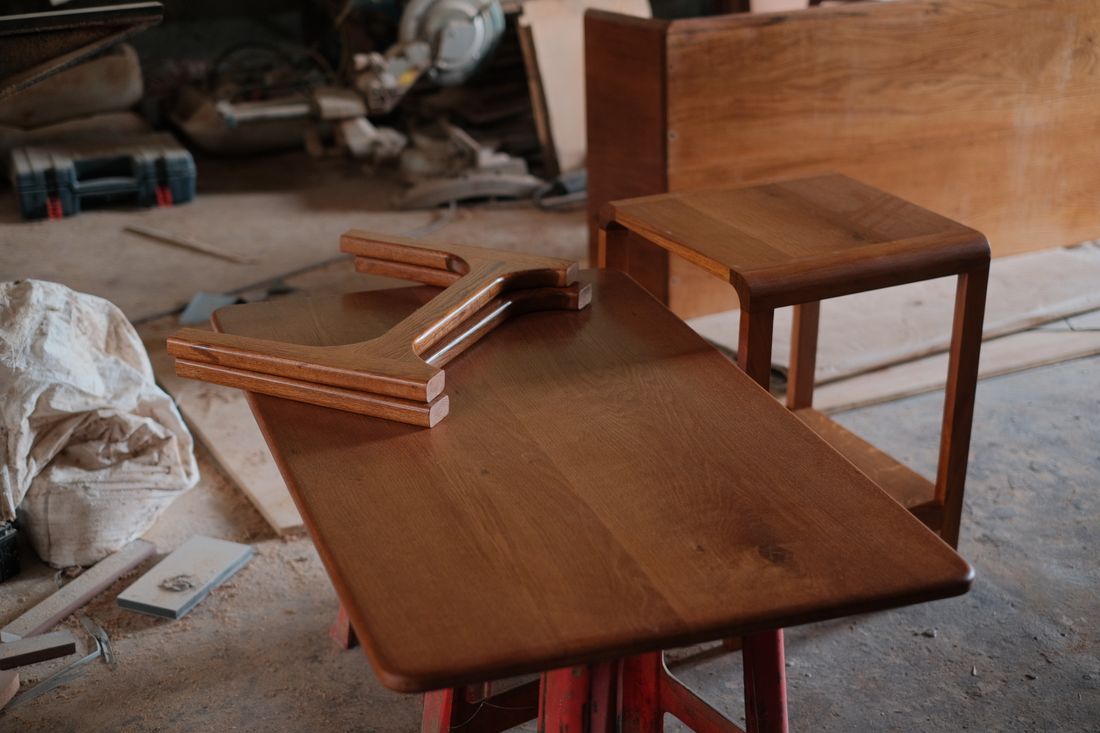 Finished wooden furniture pieces resting on a workshop table alongside tools and wood shavings
