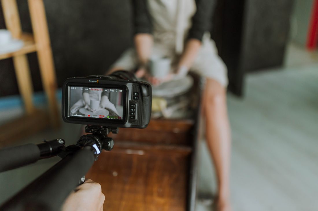 A video camera's monitor screen framing a maker working at a bench, filmed from behind the camera operator