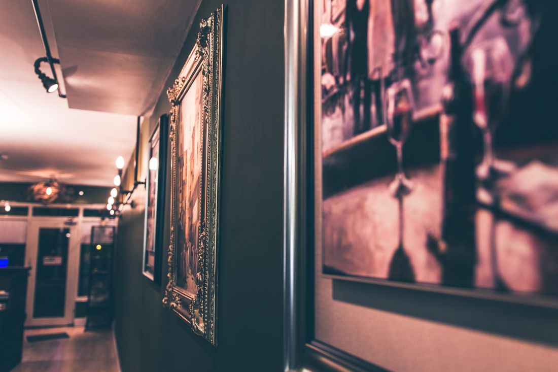A dim interior corridor with ornately framed artwork hung along the wall