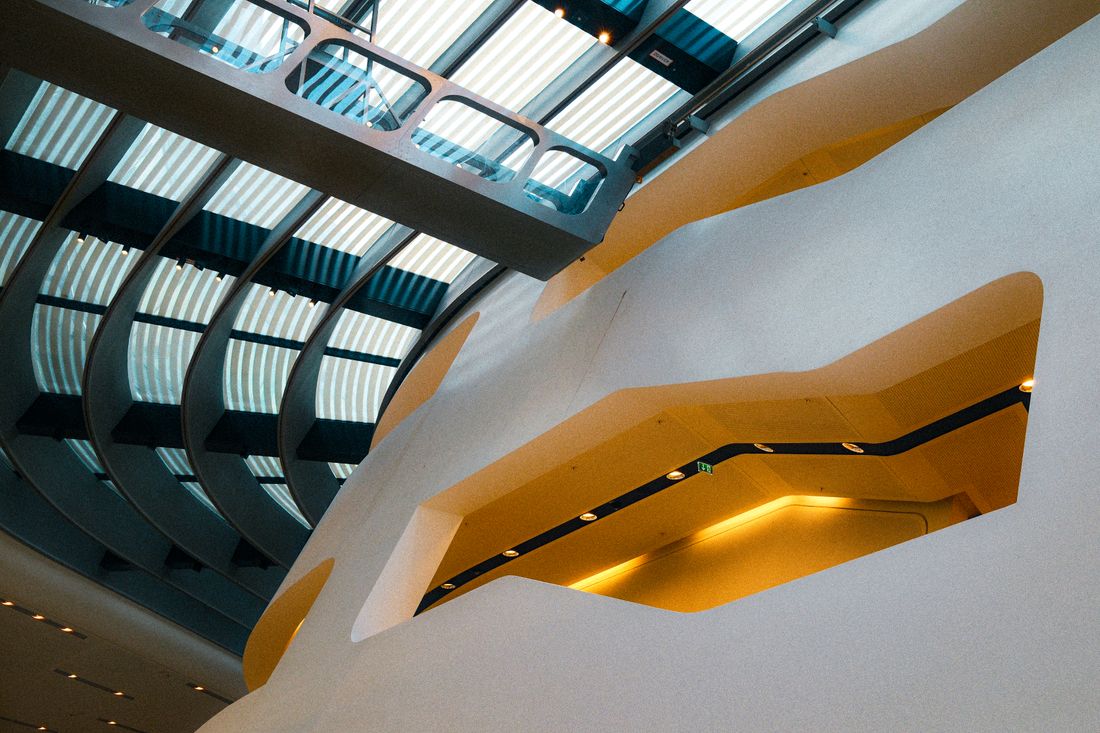 A sculptural modern building interior with a curved skylight ceiling, viewed from below