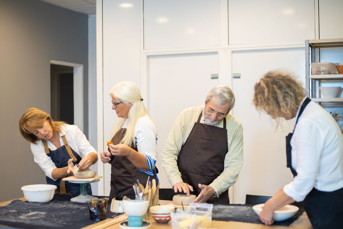 A small group of adults working together on pottery at a table in a bright community workshop room