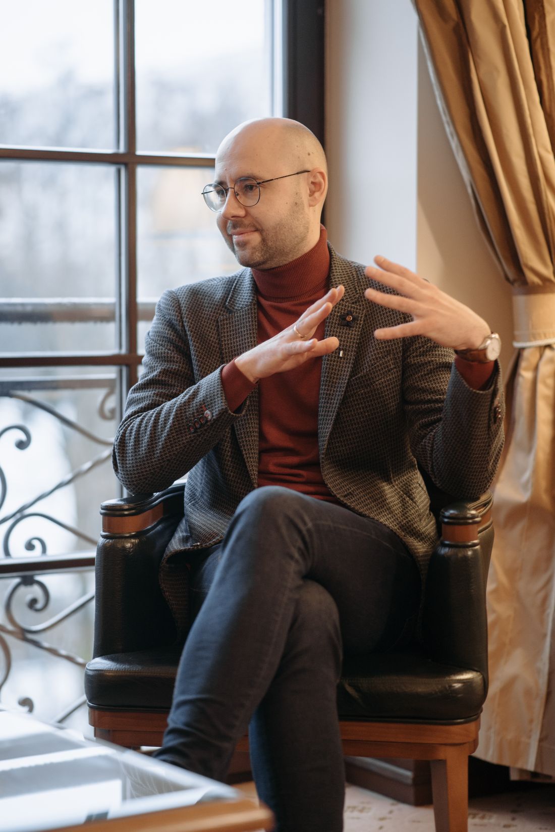 A man in a blazer speaking warmly and gesturing with both hands, as if addressing an audience