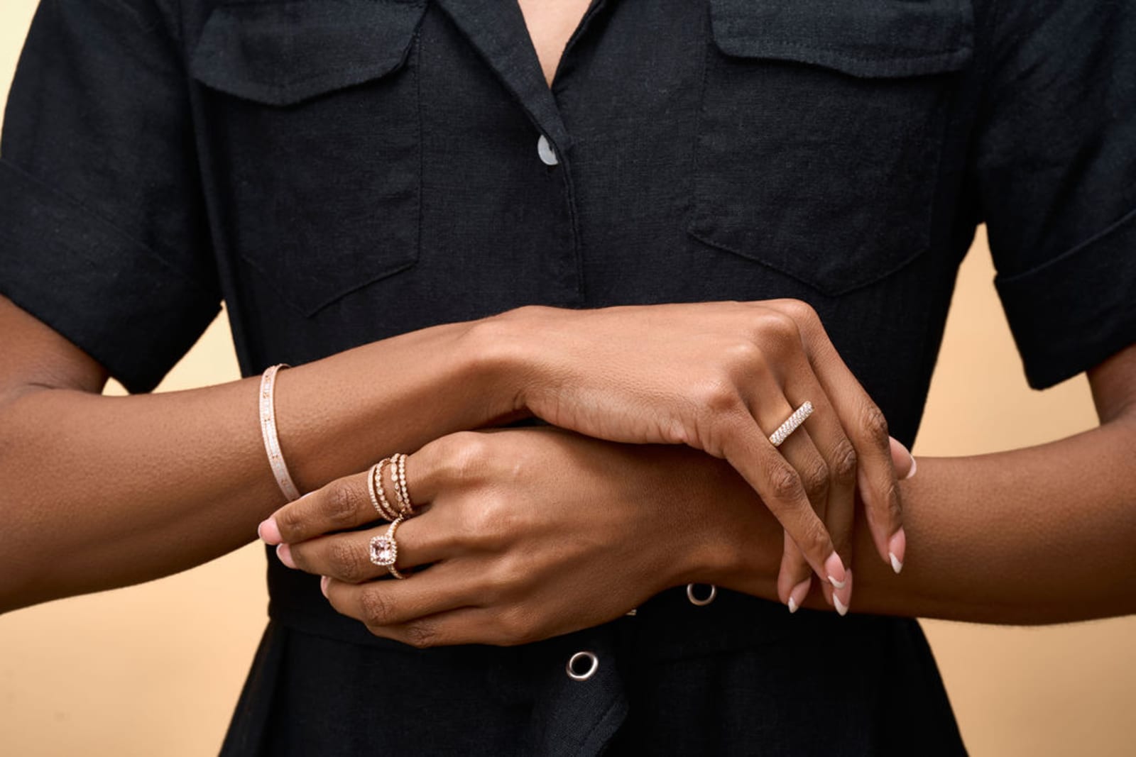 Close-up of a person's clasped hands wearing stacked rings and a thin bangle over a black linen shirt.