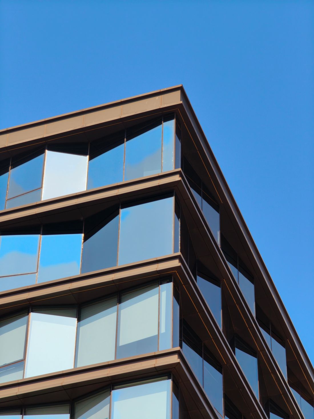 Close-up corner view of a modern glass and steel building facade against a clear blue sky
