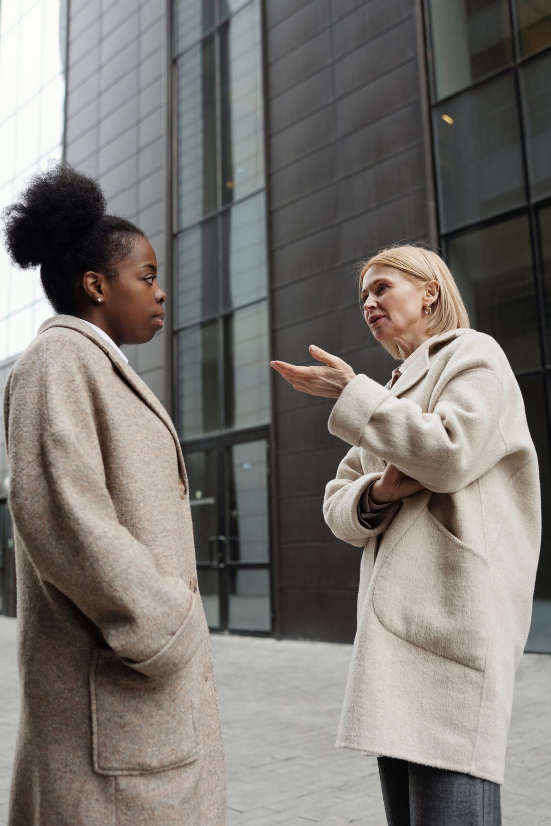 Two women in conversation standing outdoors in front of a modern office building facade