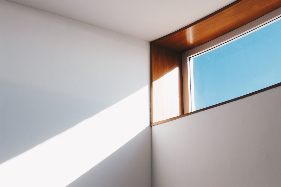 A sunlit corner of a white interior with a wood-trimmed window and clear blue sky