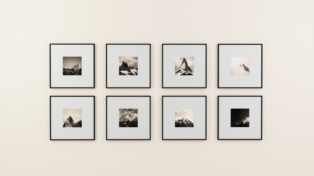 Eight small framed black-and-white mountain photographs arranged in a grid on a plain, warm-toned wall