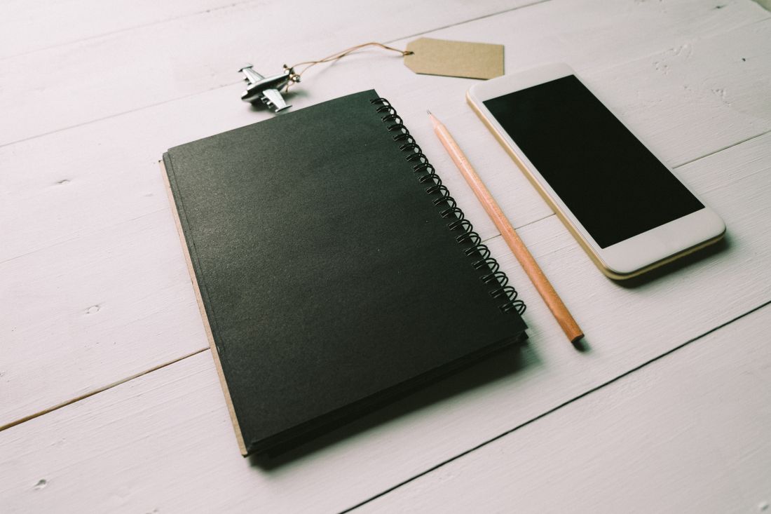 A flat lay of a spiral notebook, smartphone, and pencil arranged on a wooden desk for content planning.