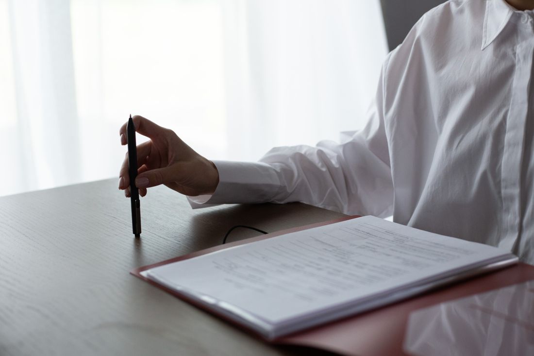 A woman examines documents, holding a pen over a table in a bright indoor setting.