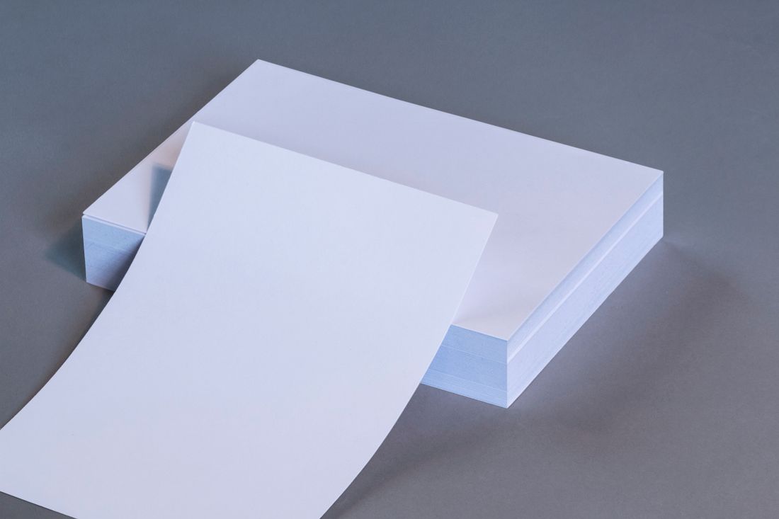 A stack of blank white paper sheets on a plain gray surface, viewed edge-on with the top sheet lifted.