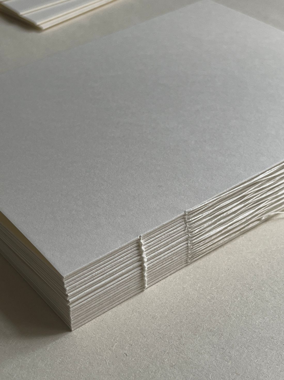 Close-up of a stack of blank paper sheets bound with thread, resting on a plain table