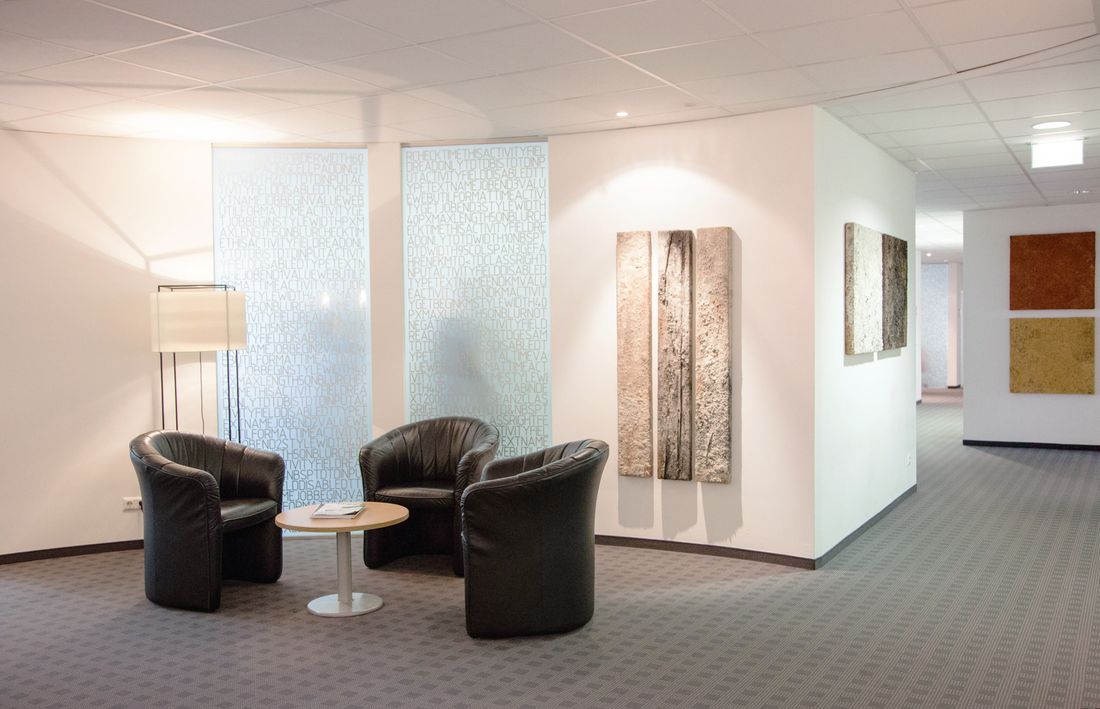 A corporate office lounge with framed abstract artwork on the wall beside leather seating and a corridor beyond