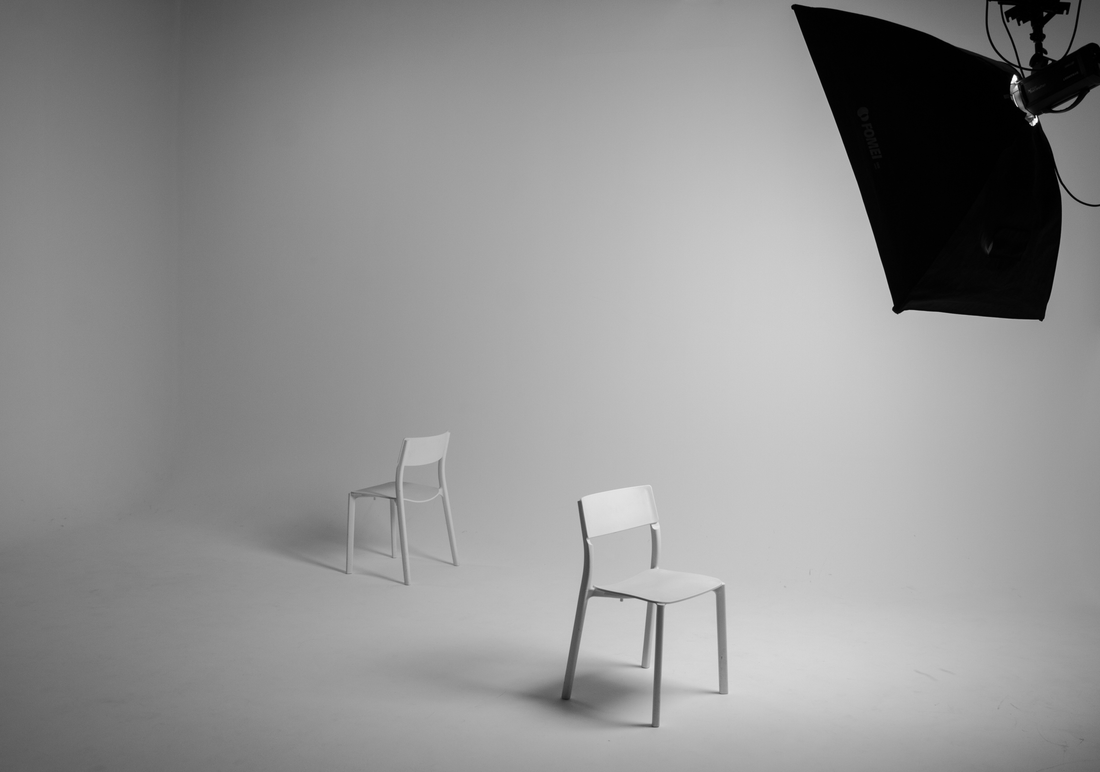 Two empty chairs facing each other in a minimalist grayscale studio with a softbox light overhead