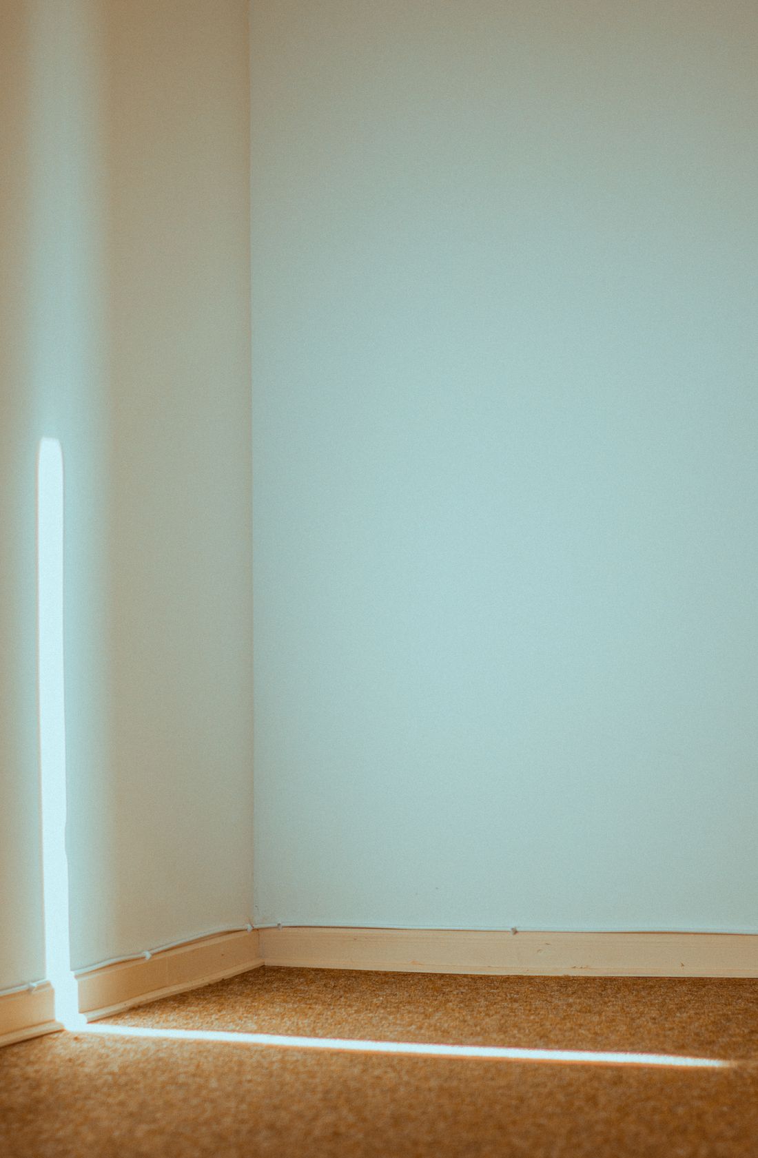 A quiet beam of window daylight falling across the corner of an empty room