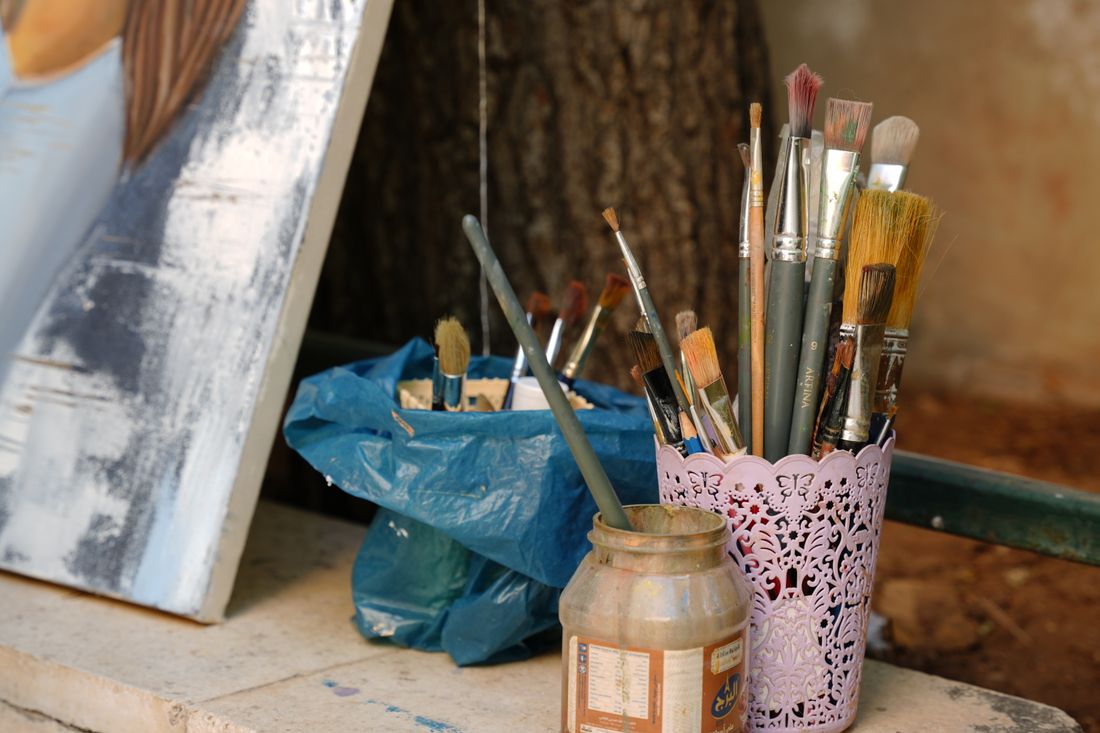 A jar of brushes, jars and a leaning canvas in the corner of a working studio