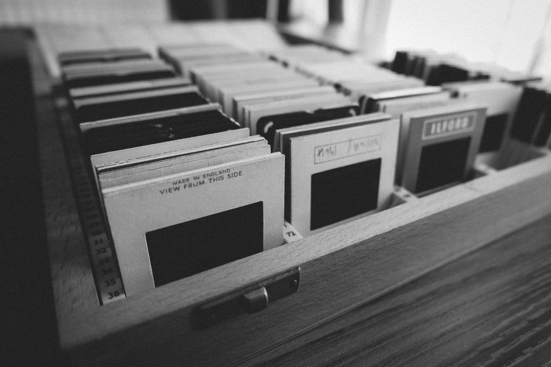 A wooden drawer of vintage photographic slides in individual paper sleeves, photographed in black and white