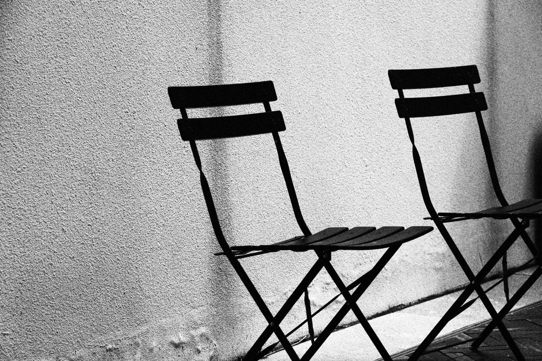 Two matching folding chairs standing side by side against a wall, casting equal shadows in black and white