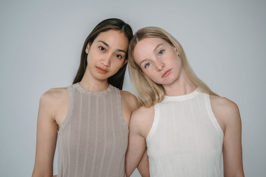 Two women standing close together against a plain neutral background, both facing the camera with equal visual weight