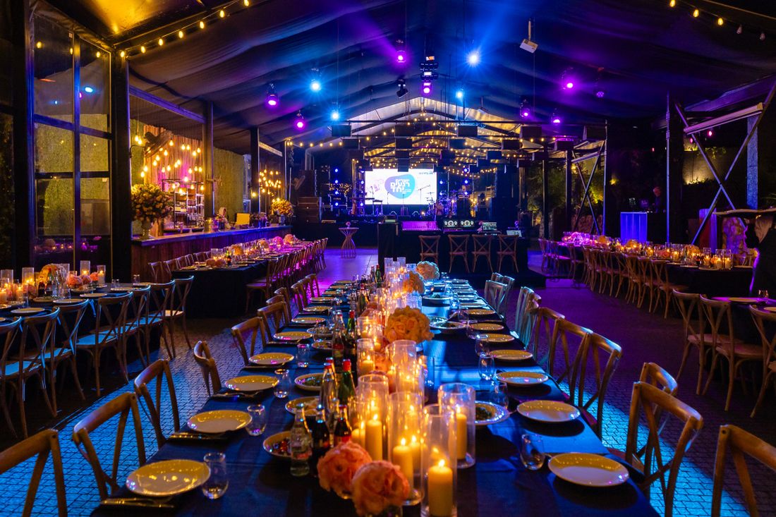 Candlelit tables set for an evening gala reception with a stage visible in the background