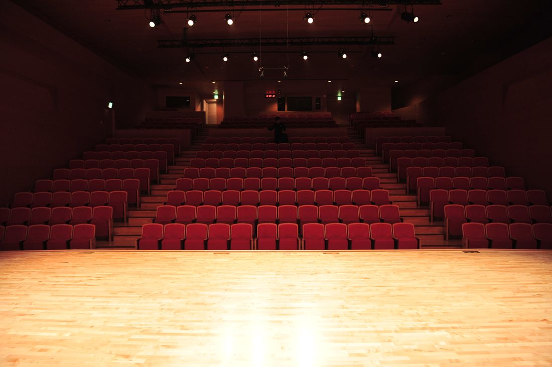 Empty theater stage with rows of red seats, lit before an evening program begins