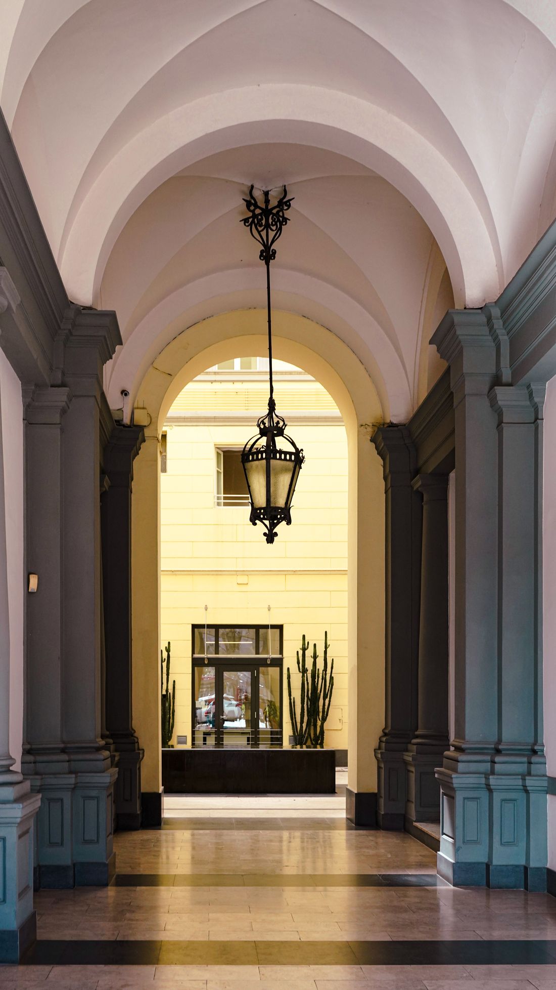 An arched interior corridor in an older building, leading toward a sunlit courtyard entrance