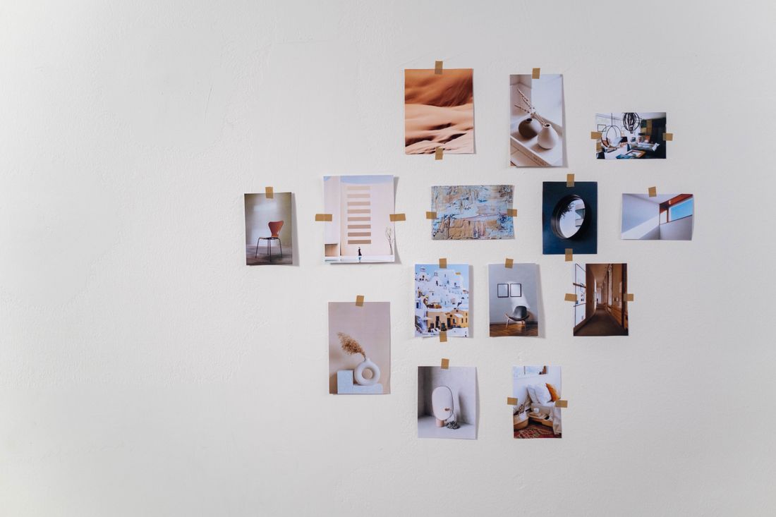 A grid of small printed photographs taped to a plain white wall, showing muted interior and texture images with no identifiable people or readable text.