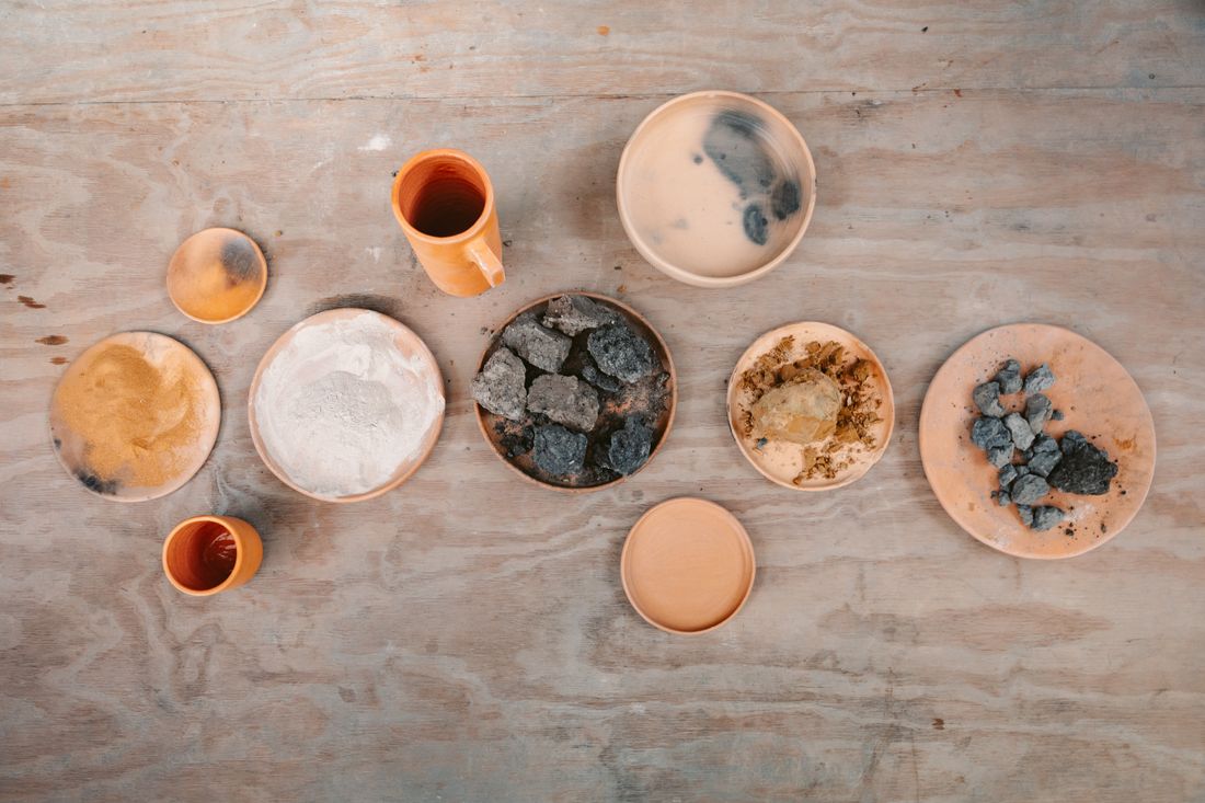 Small bowls of natural pigments and raw material samples arranged on a wooden surface