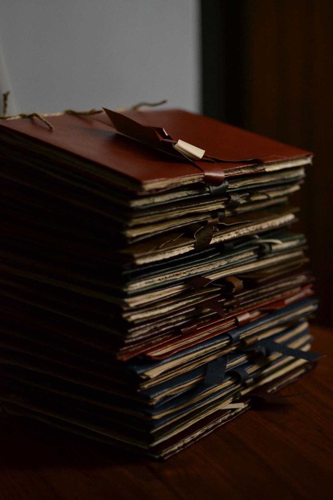 A tall stack of worn file folders tied closed with cord, resting on a wooden desk