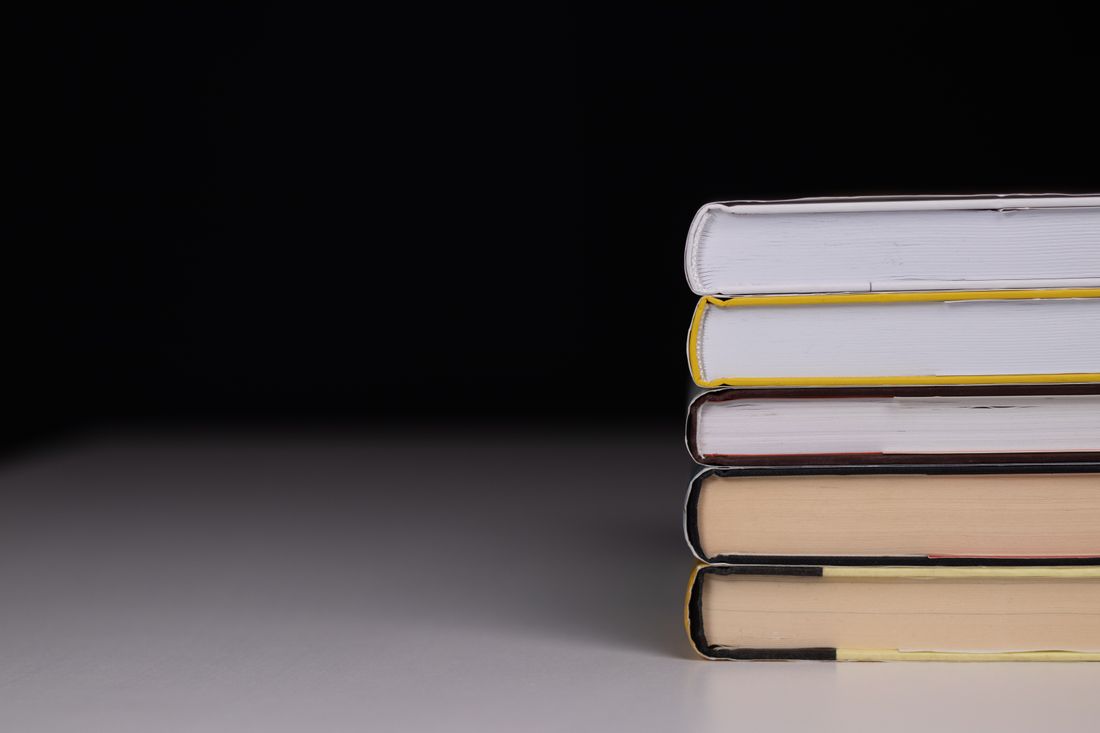 A neat stack of hardcover books with blank spines against a dark background