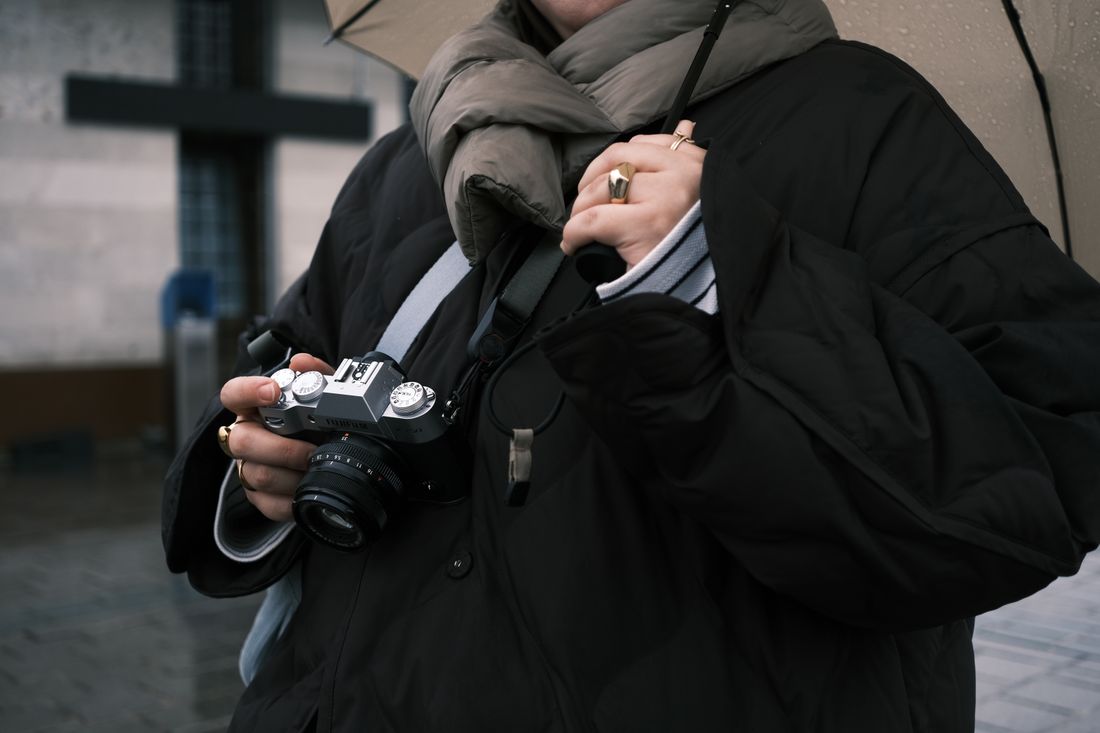 A person holding a camera under an umbrella on a rainy day
