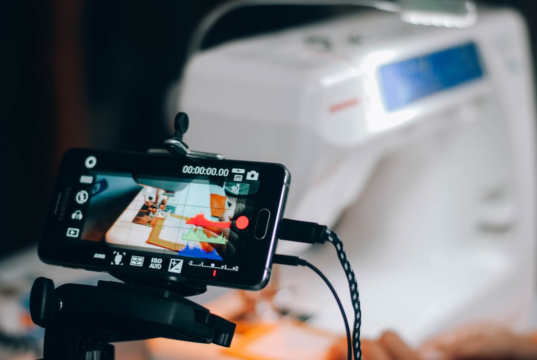 A smartphone on a tripod recording a sewing machine mid-process