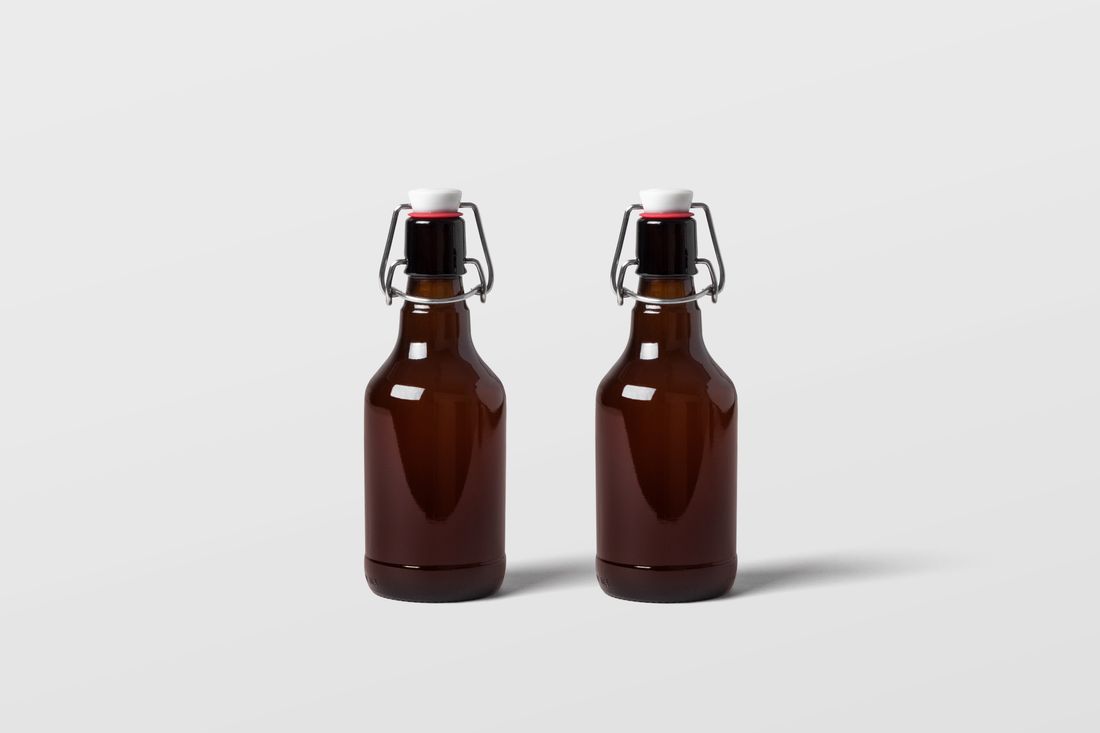 Two unlabeled amber glass bottles with swing-top caps standing side by side on a plain light gray backdrop, evenly lit catalog-style product photography.