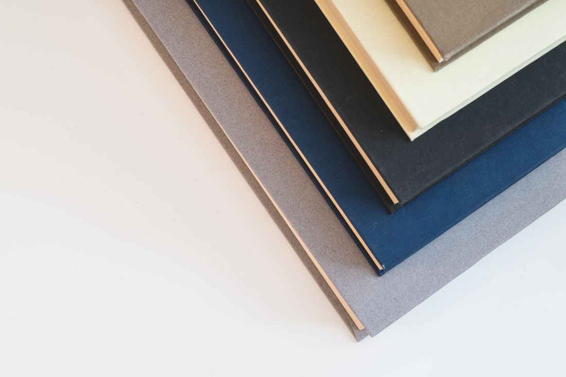 A stack of hardcover books with different colored covers arranged at an angle on a plain surface