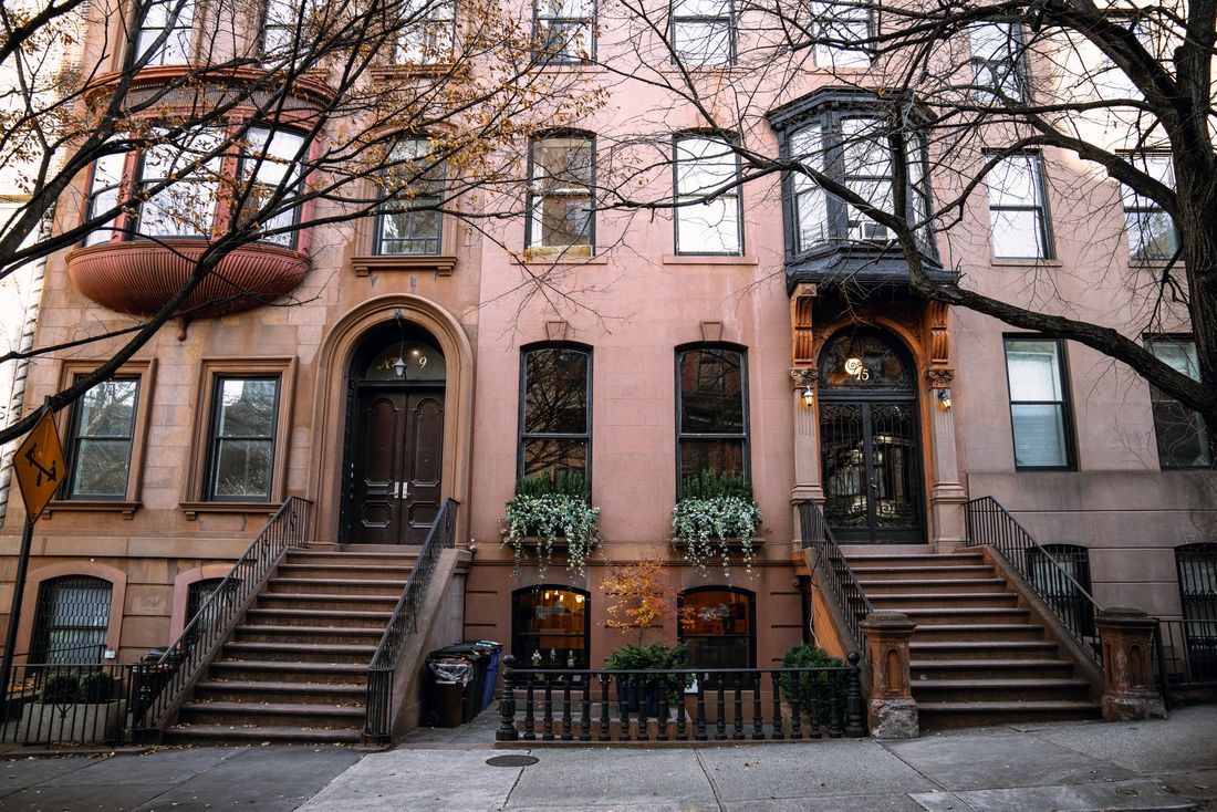 A row of Brooklyn brownstones with tall stoops and bare autumn trees along a quiet sidewalk.