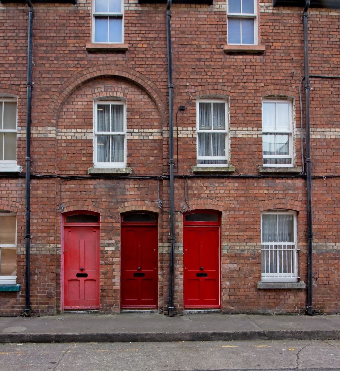 A row of three matching red entrance doors set into a brick building facade