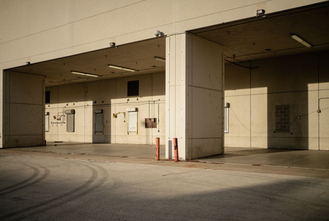 An empty concrete loading bay with two roll-up doors and worn walls, seen straight on in daylight