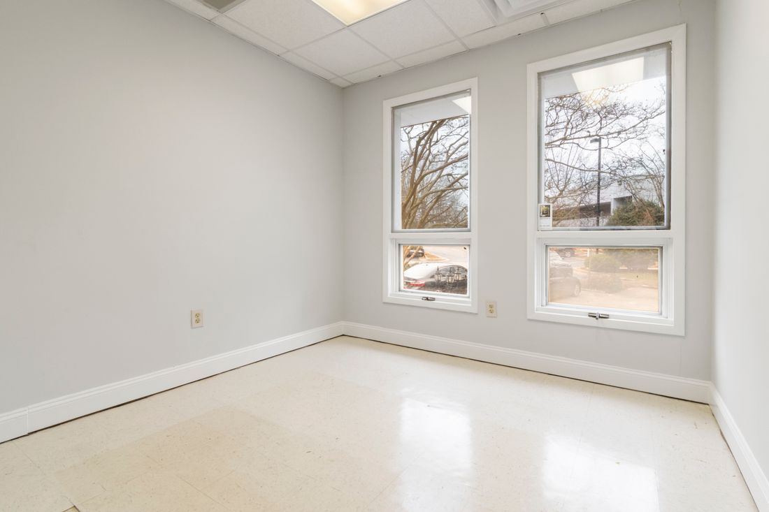 A bright, empty room in a commercial building with a clean tile floor and two windows letting in daylight