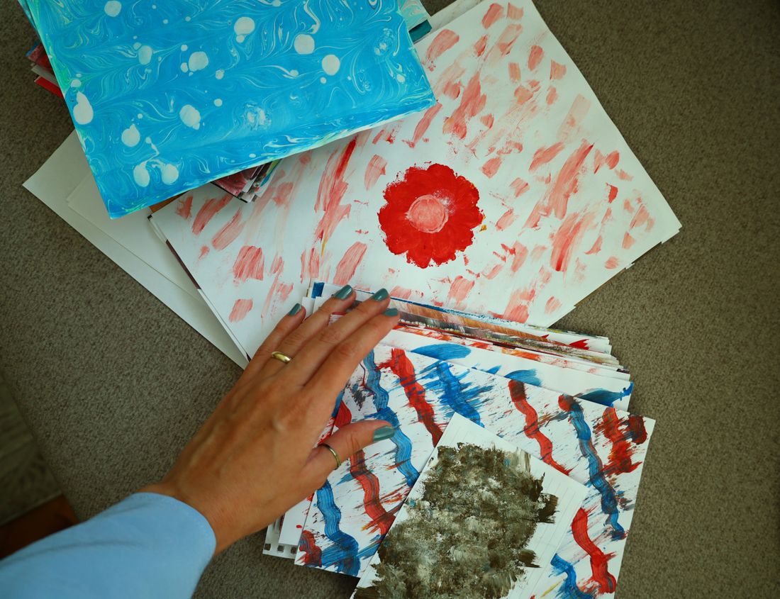 A stack of small works on paper seen from overhead, a hand reaching in to lift the top sheet