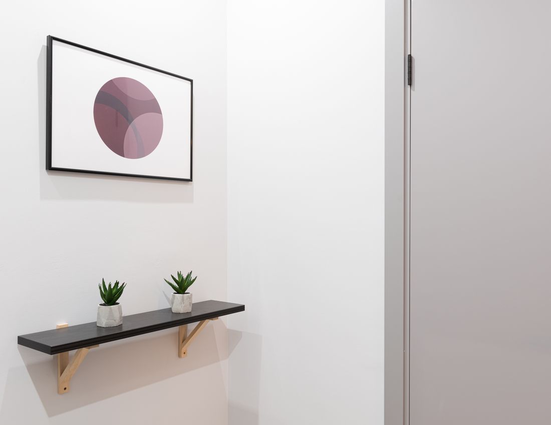A single small framed abstract print centered on a plain wall with generous empty space around it