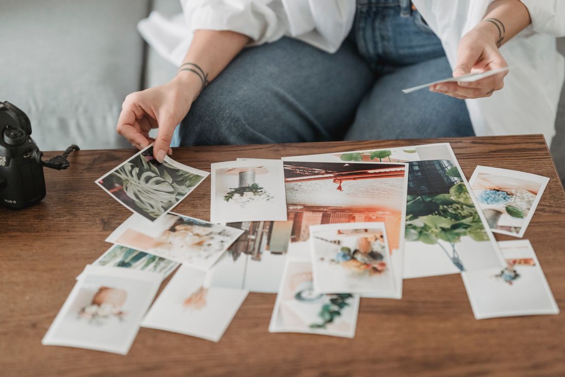 Several printed photographs of different framings laid out on a table, a hand placing one print among the others.