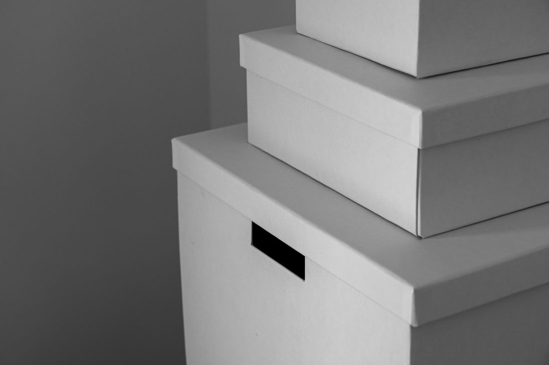 A small stack of unlabeled white storage boxes in the corner of a plain room, shot with shallow depth of field