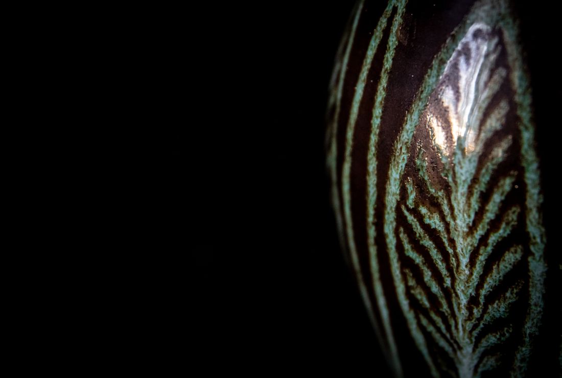 Close-up of a dark glossy ceramic surface with a bright blown-out specular highlight where the light source reflects directly off the curved glaze
