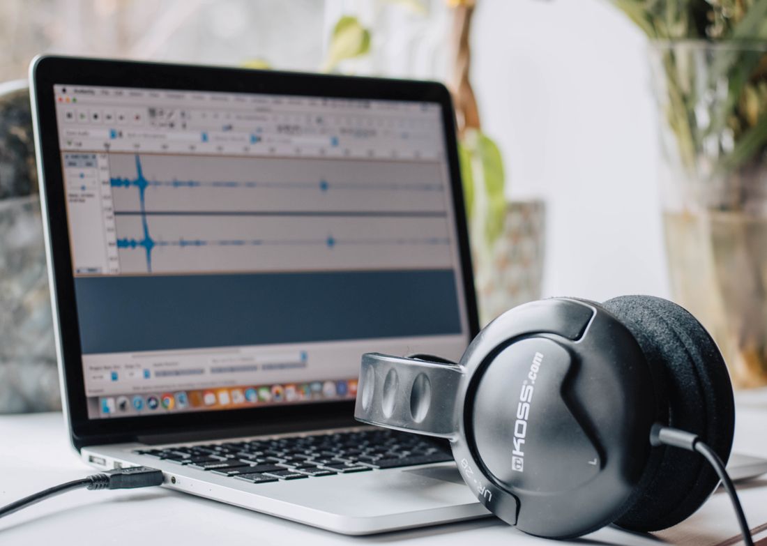 Headphones resting on a laptop keyboard next to an open audio-editing waveform
