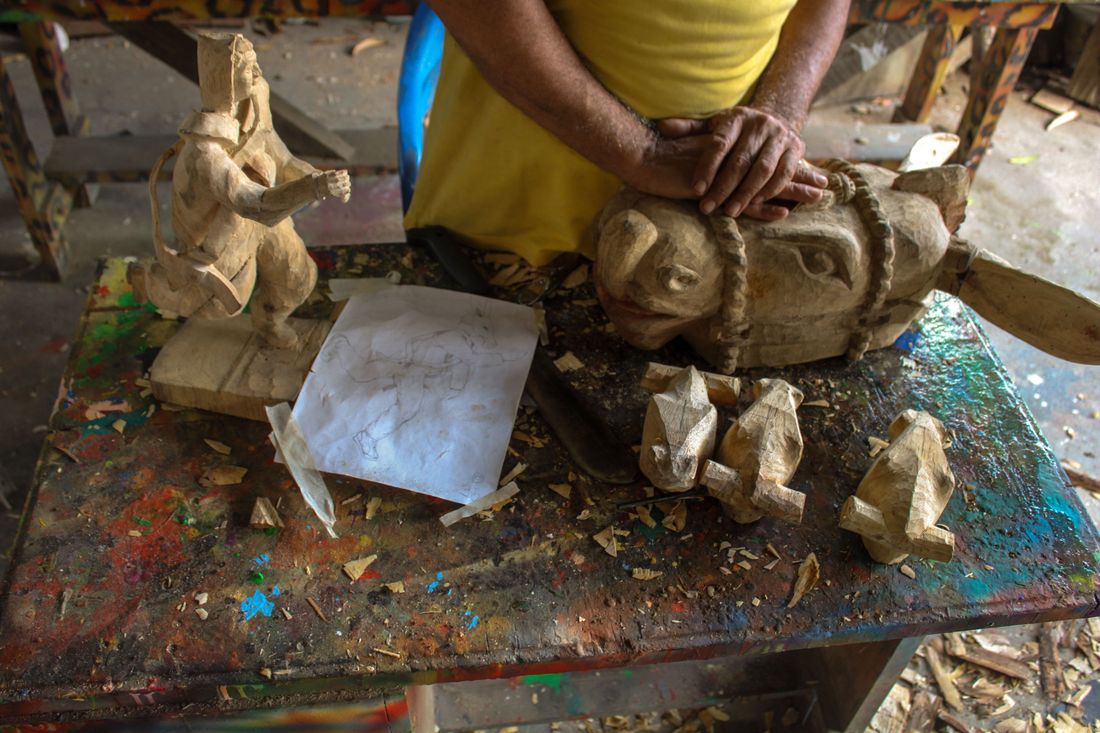 Hands crafting a small wooden sculpture at a paint-splattered workshop table