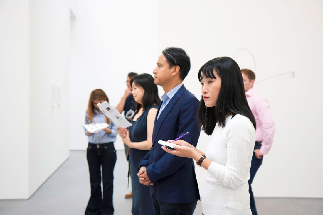 A small group of gallery visitors standing close together, attentively looking at something off-frame