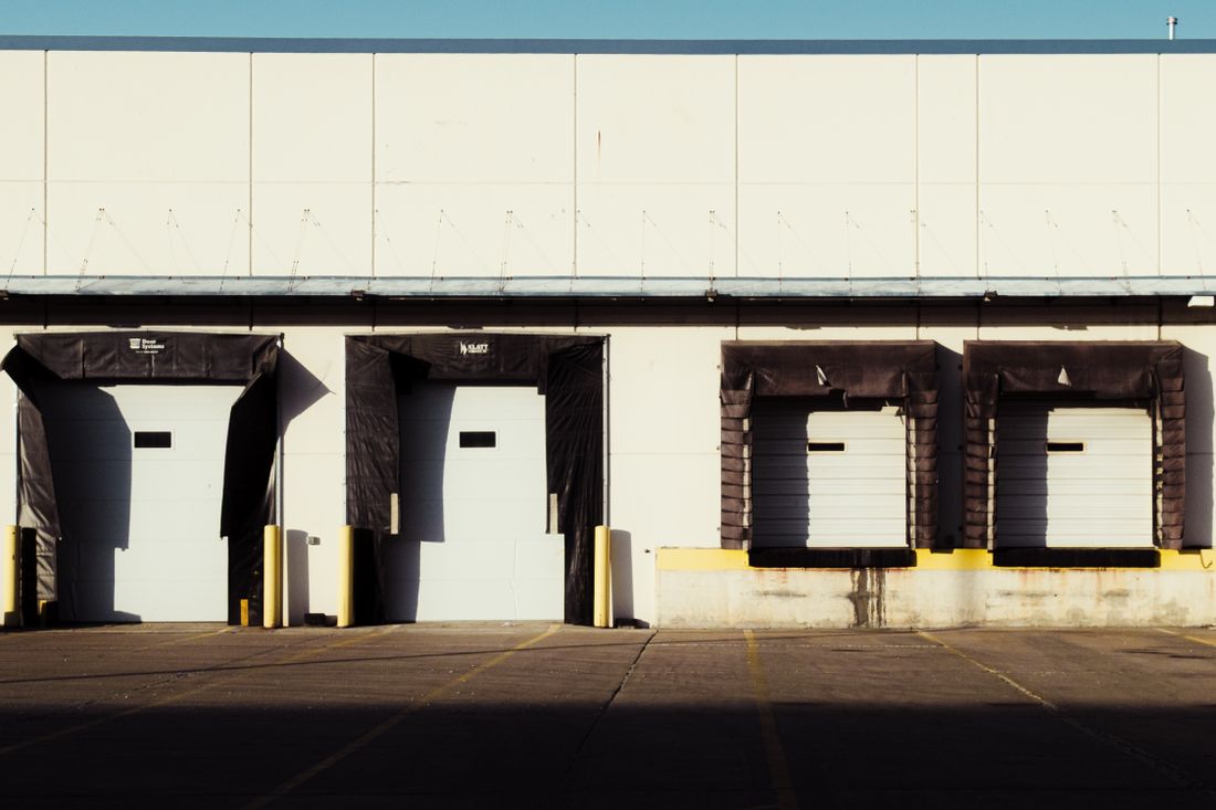 An industrial loading dock with closed bay doors in daylight