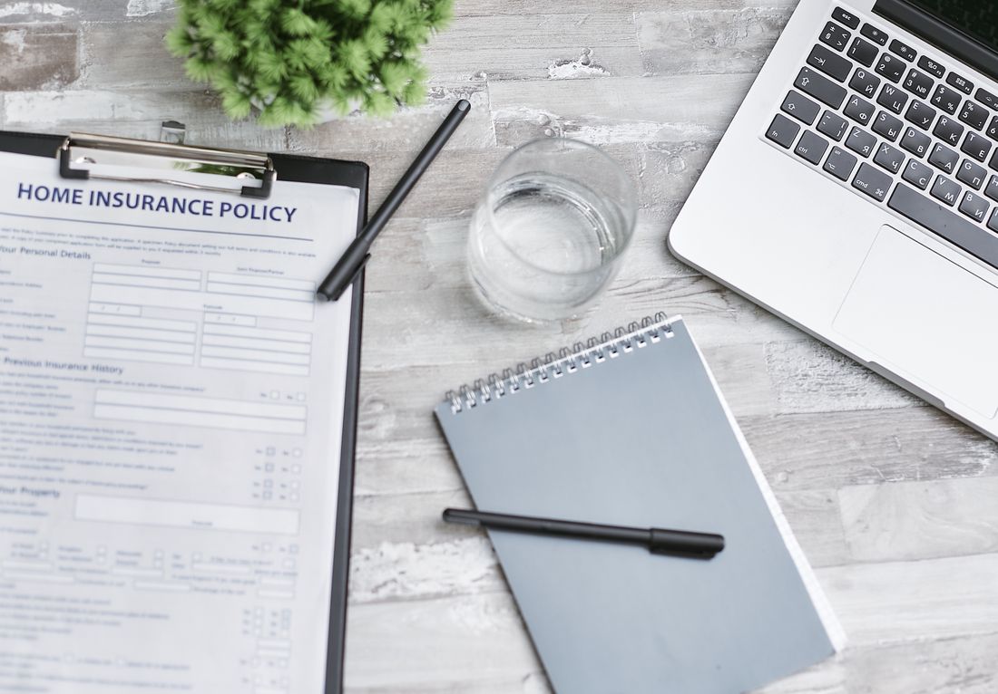 A flat lay of an insurance document, laptop, and notebook arranged on a desk
