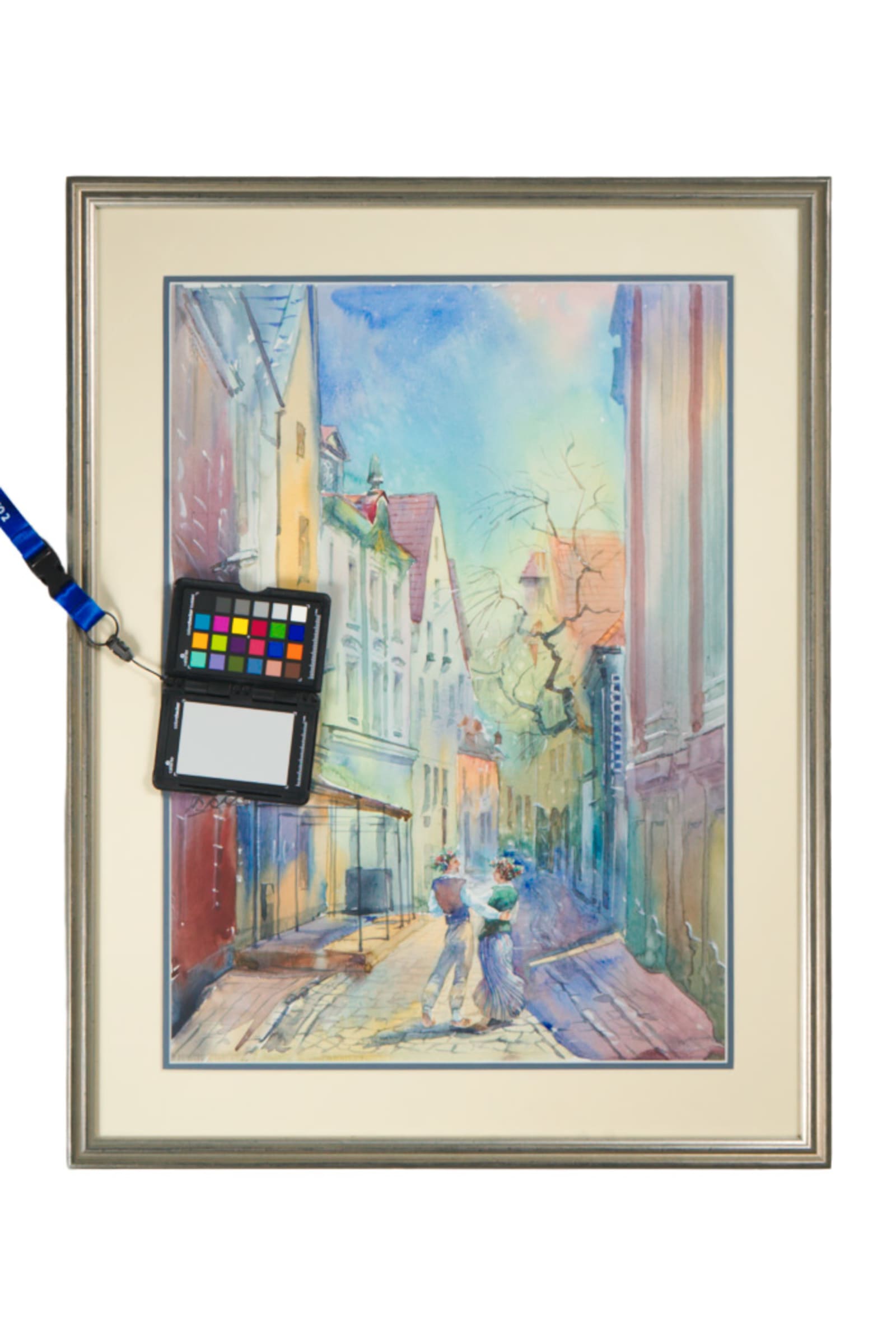 A framed watercolor street scene photographed with a color-calibration card and grey card in frame for color-accurate documentation