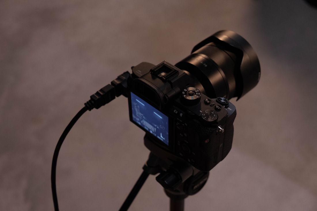 A camera mounted on a tripod with a tethered cable, its screen showing a captured image during a documentation shoot